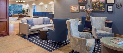 A spacious lobby with a stone floor, a blue and white striped rug, a gray sofa, and a blue armchair.