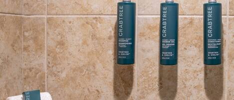 Tres botellas de champú y acondicionador de Crabtree & Evelyn sobre una pared de azulejos.