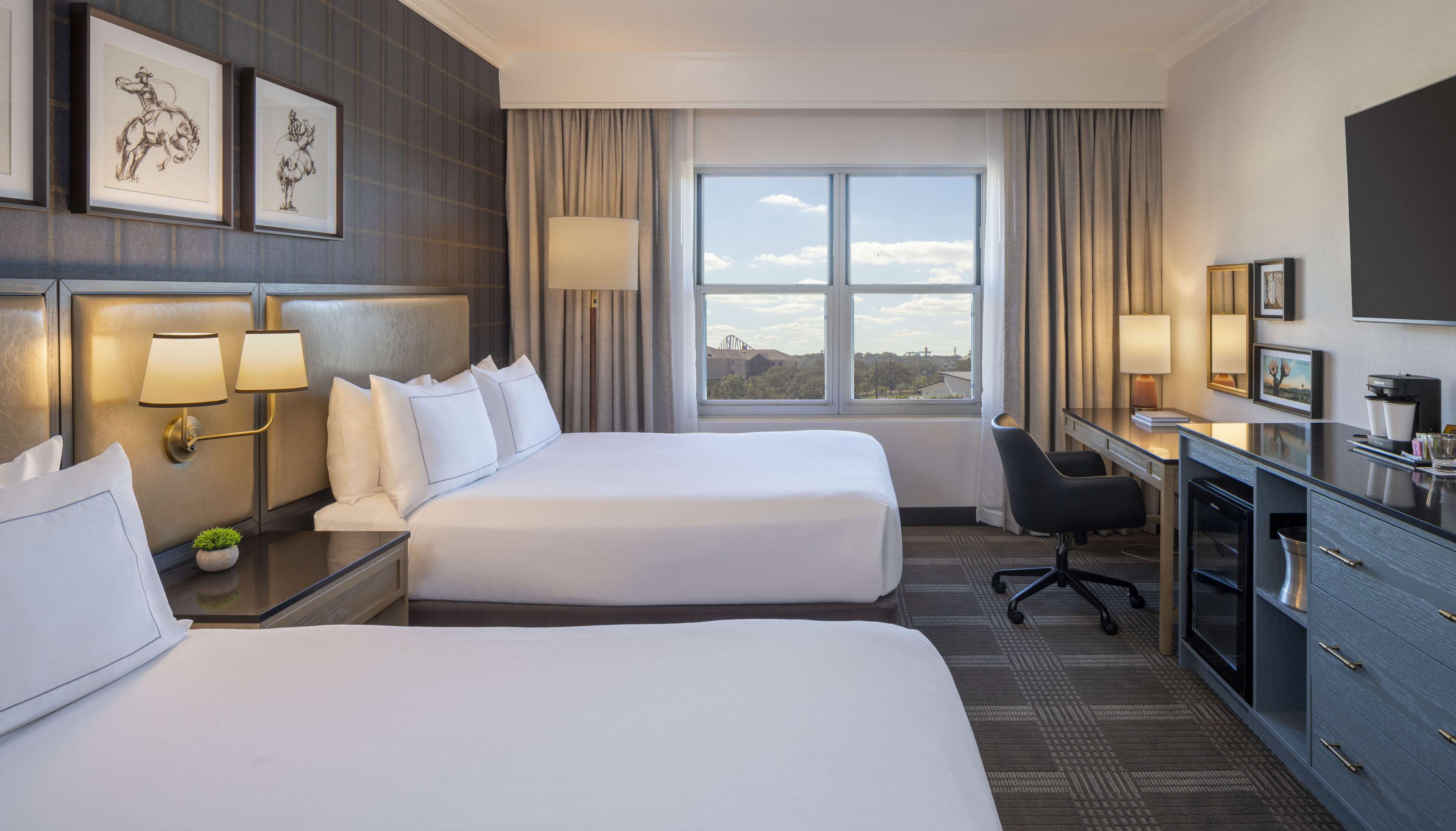 Une chambre d’hôtel avec deux lits, un bureau, une chaise et une grande fenêtre donnant sur un paysage agréable.