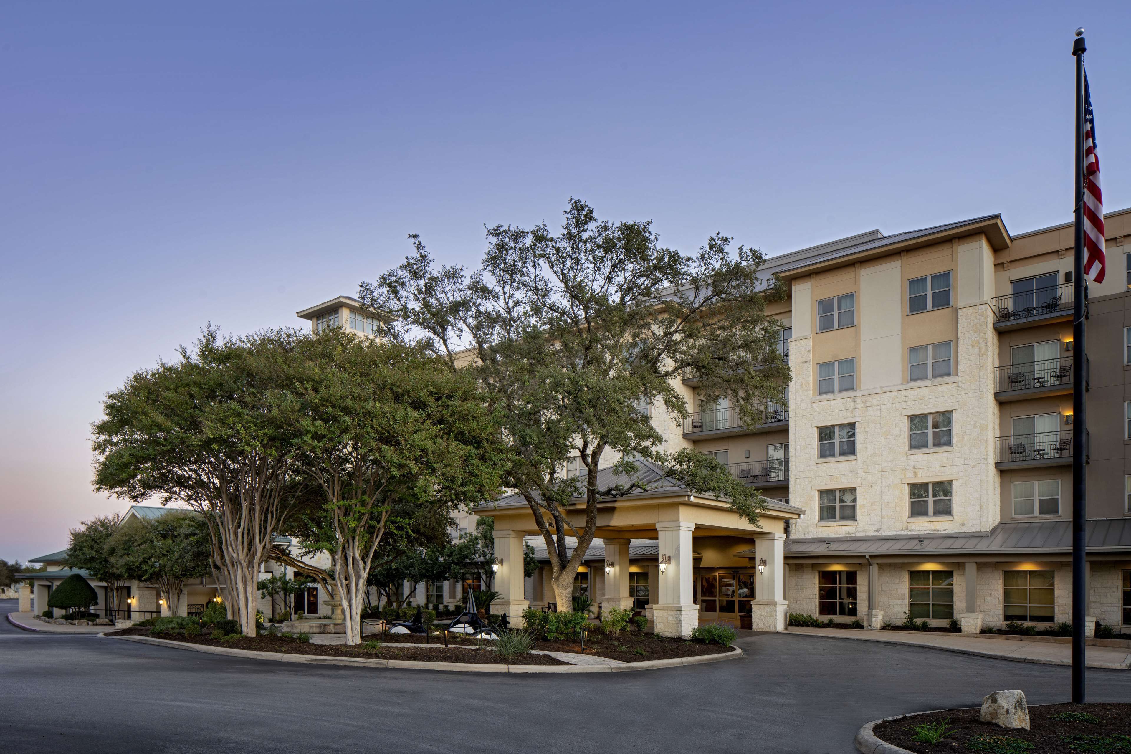 A multi-story hotel with a central courtyard, outdoor seating, and a flagpole.