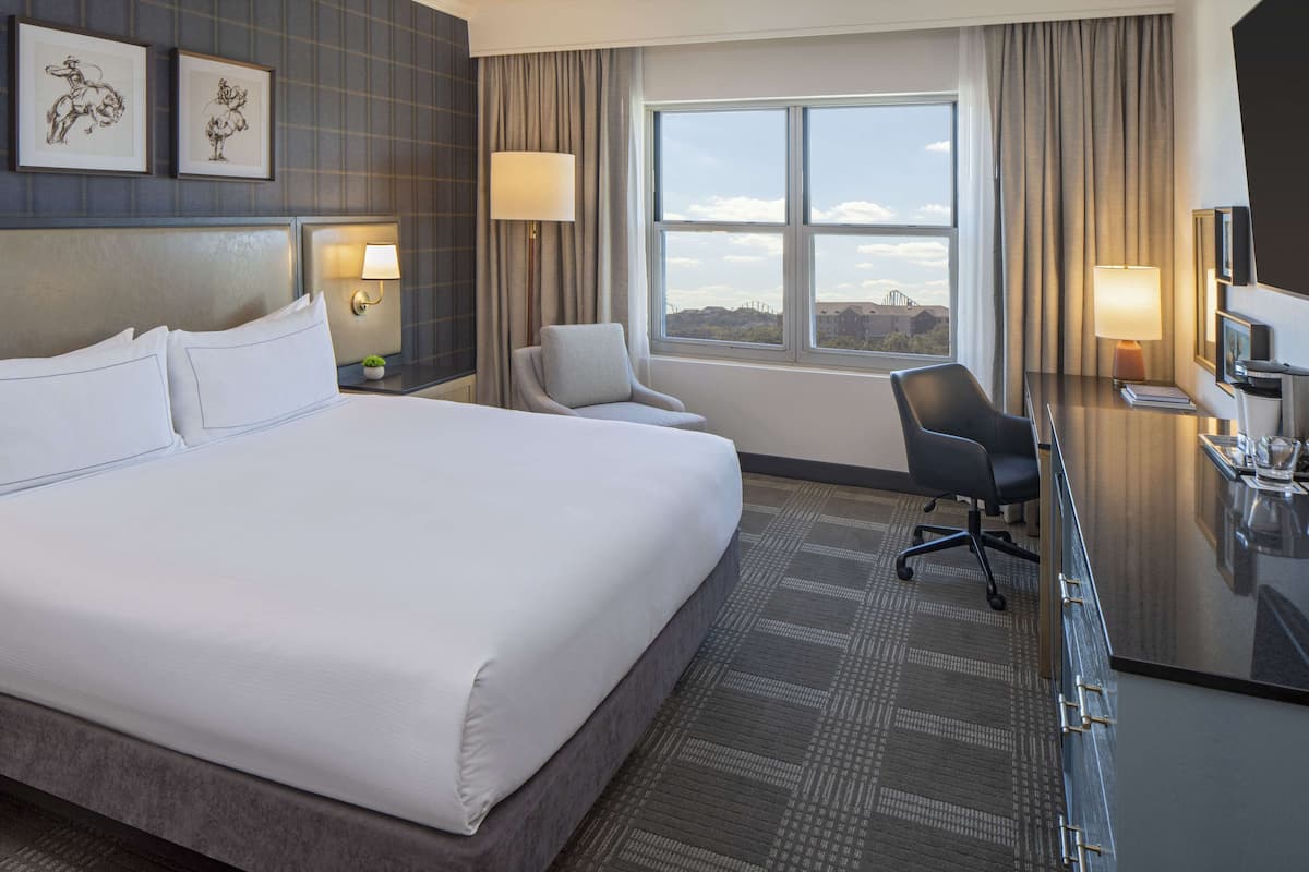 A hotel room with a large bed, a desk with a chair, a TV, and a window with a view.