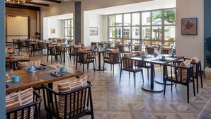 A spacious dining area with multiple tables and chairs, large windows, and a modern ceiling design.