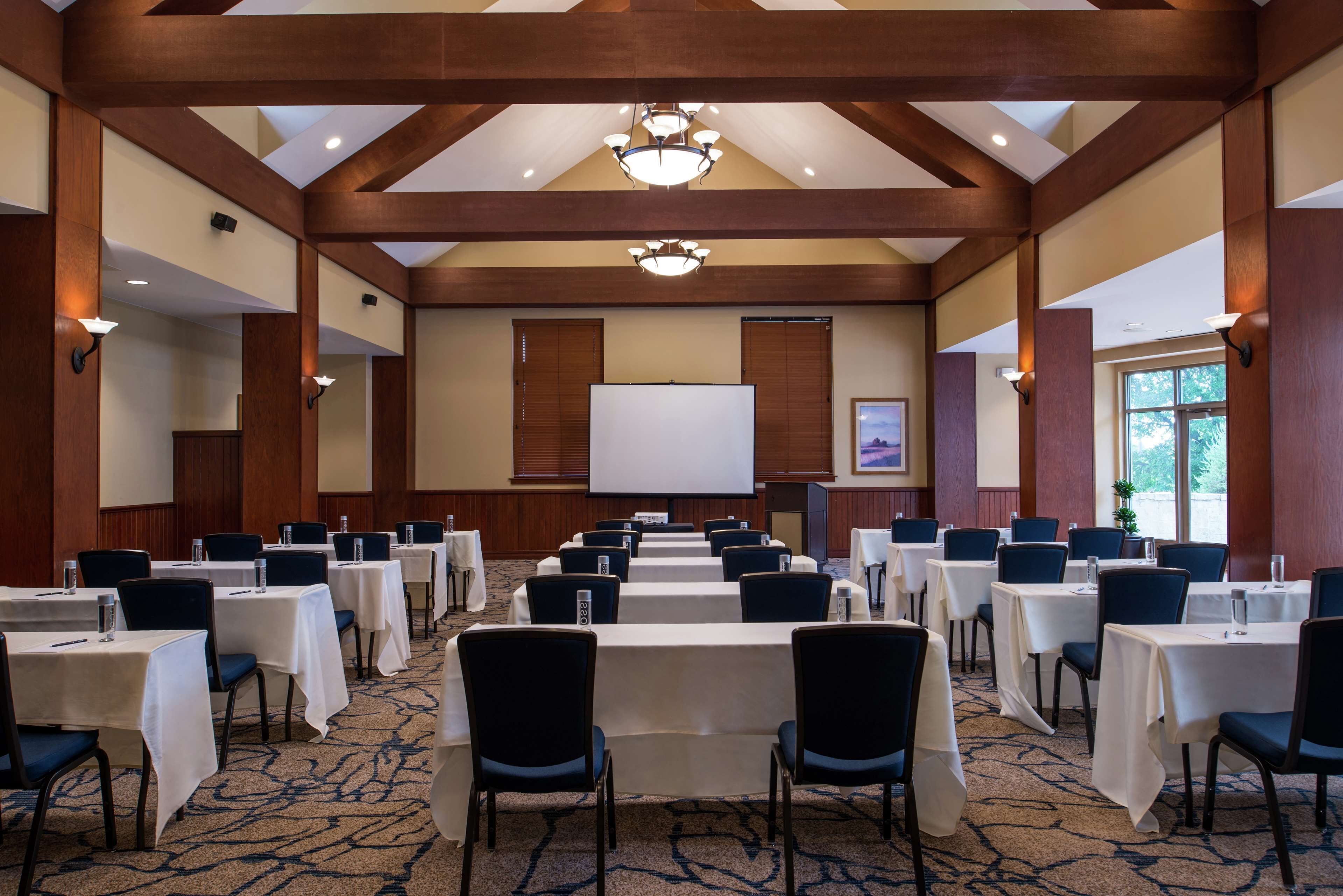 A conference room with rows of tables and chairs, a projector screen, and a large window.