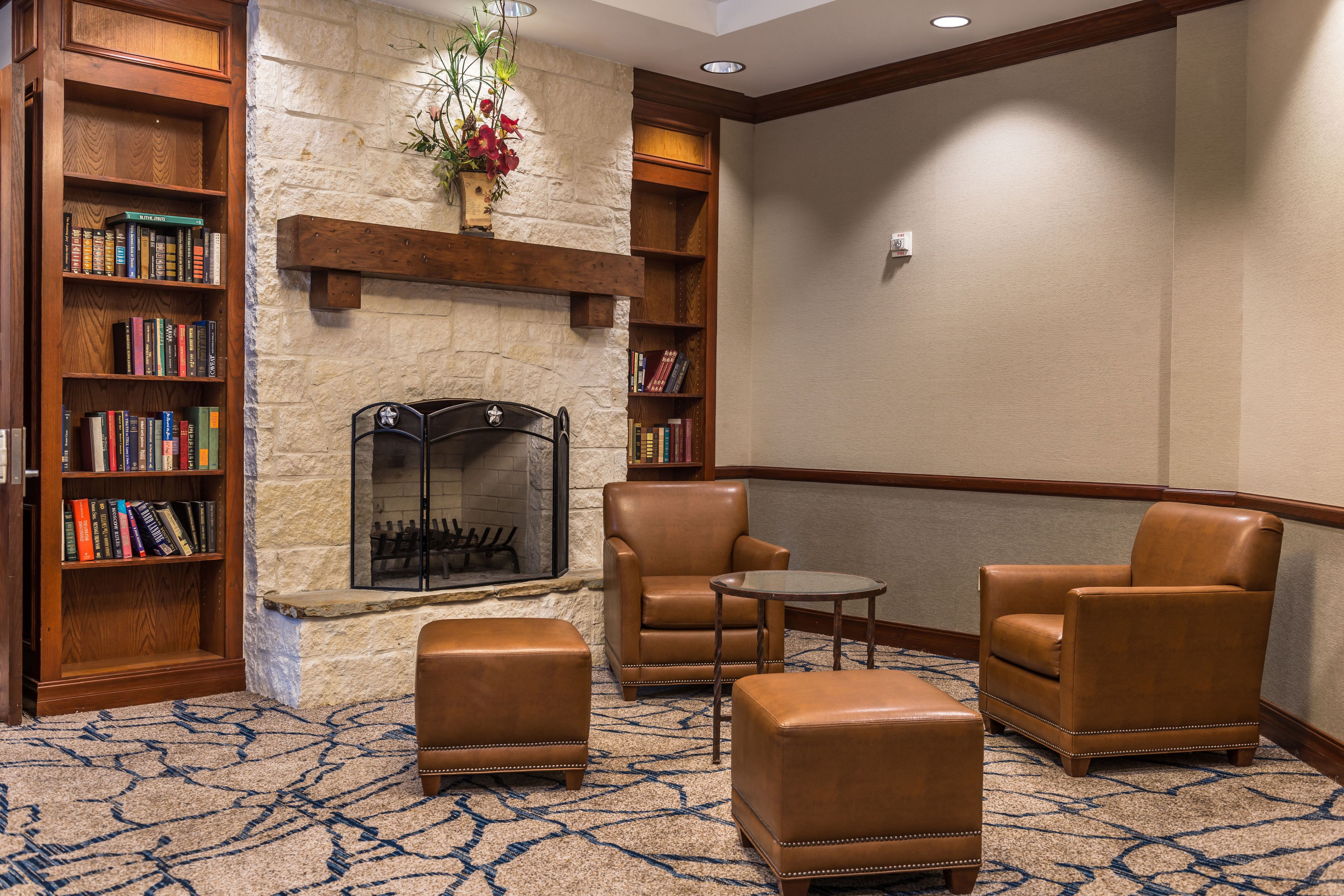 A lobby with a stone fireplace, leather armchairs, a small table, and bookshelves filled with books.