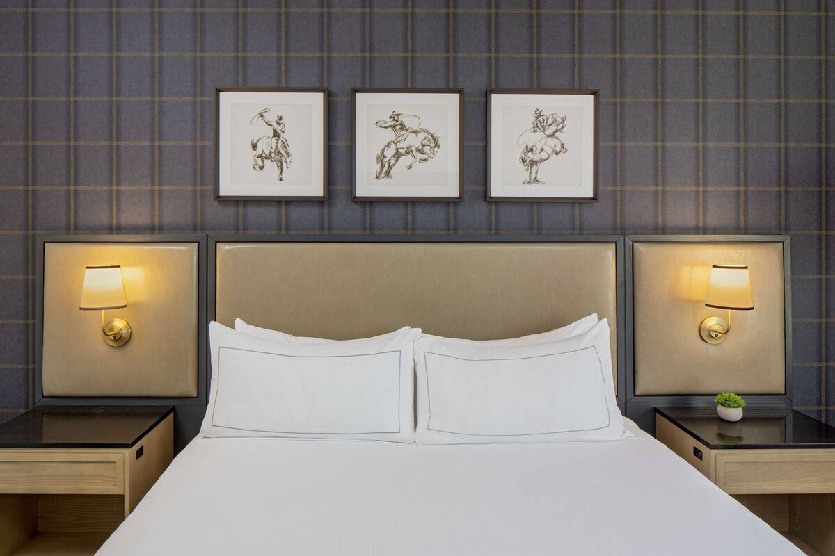 A hotel room with a large bed, two bedside tables with lamps, and three framed pictures on the wall.