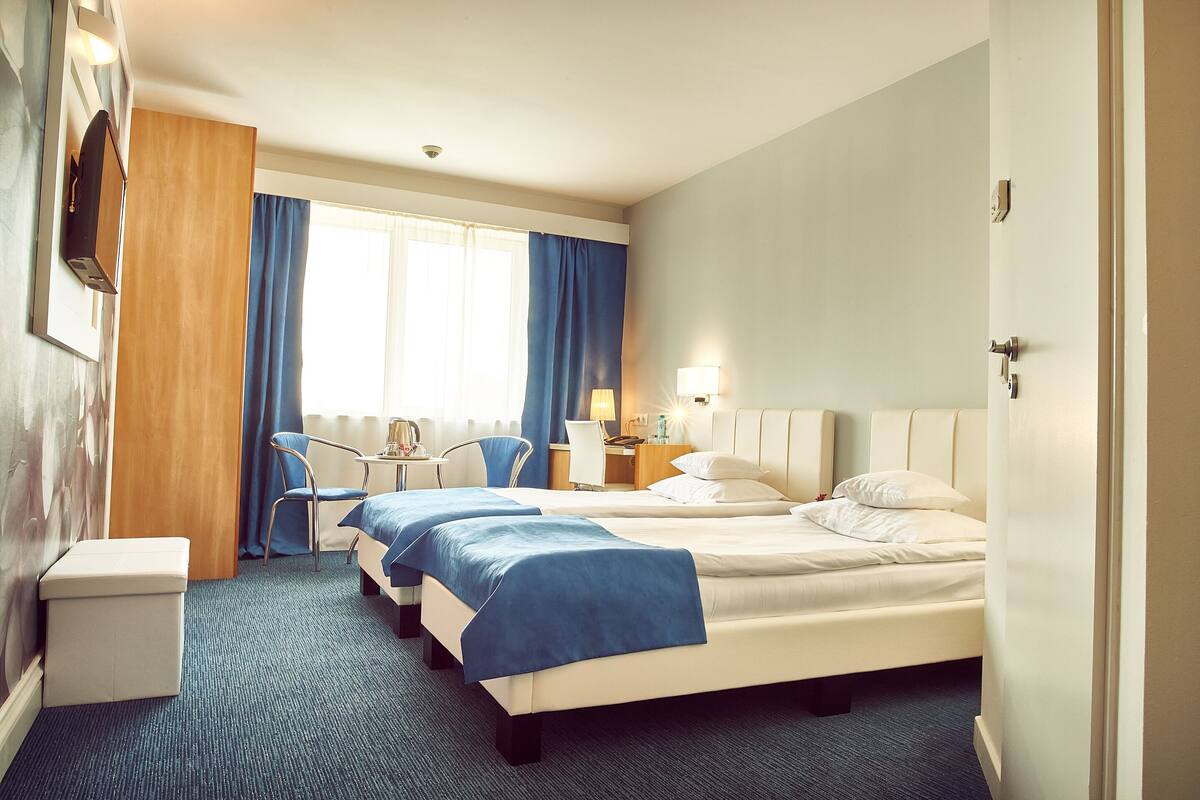 A hotel room with two beds, a desk, a chair, a small table, and a bathroom area.