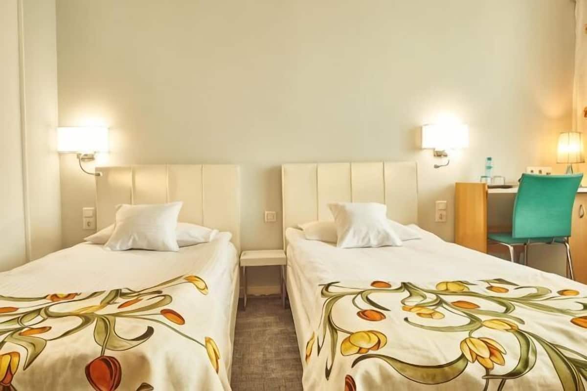 A hotel room with two beds, each with a floral bedspread, a desk with a chair, and wall-mounted lamps.