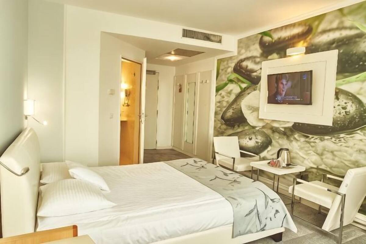 A hotel room with a bed, a TV mounted on the wall, a small table, and a chair.