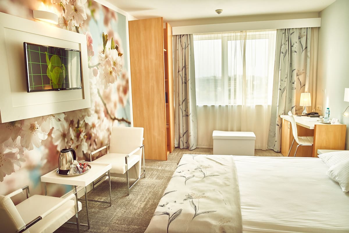 A hotel room with a bed, a desk, a chair, a TV, and a window with curtains.