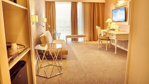 Une chambre d’hôtel avec un canapé, un bureau, une télévision et une fenêtre avec des rideaux.