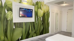Une chambre d’hôtel avec une grande fresque murale représentant des feuilles vertes, un téléviseur à écran plat fixé au mur et un lit avec une literie blanche.