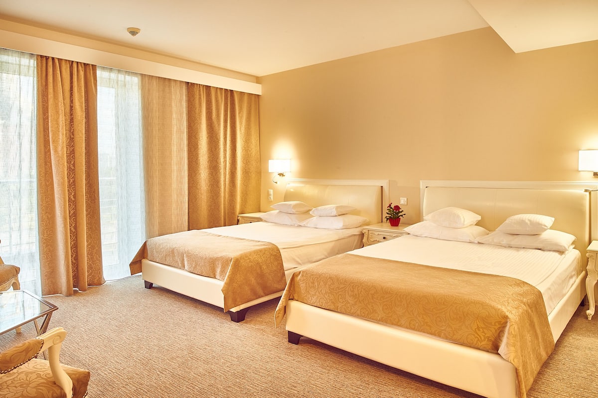 A hotel room with two beds, a sitting area, and a large window with curtains.