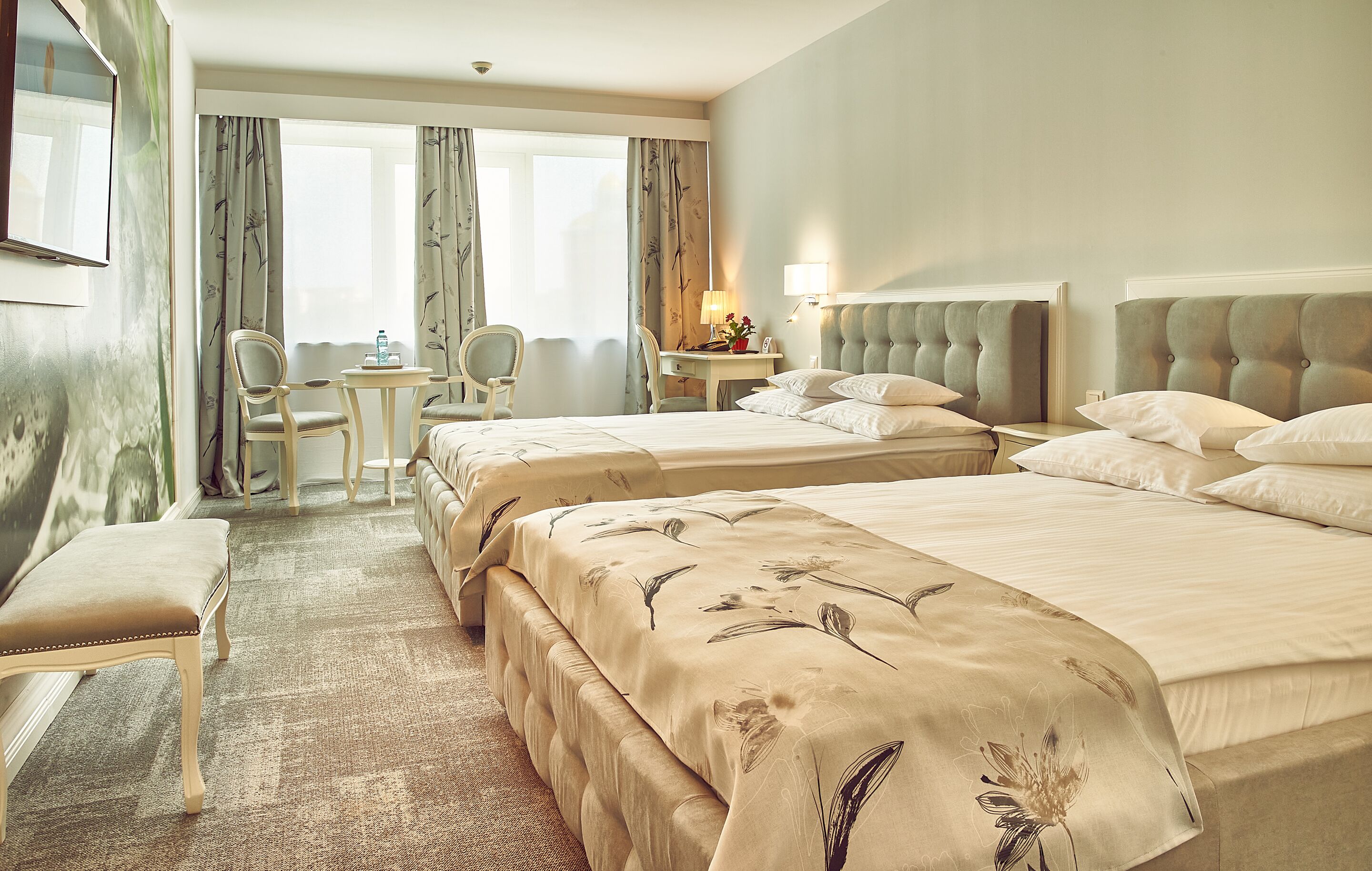A hotel room with two beds, a desk, a chair, and a large window with curtains.