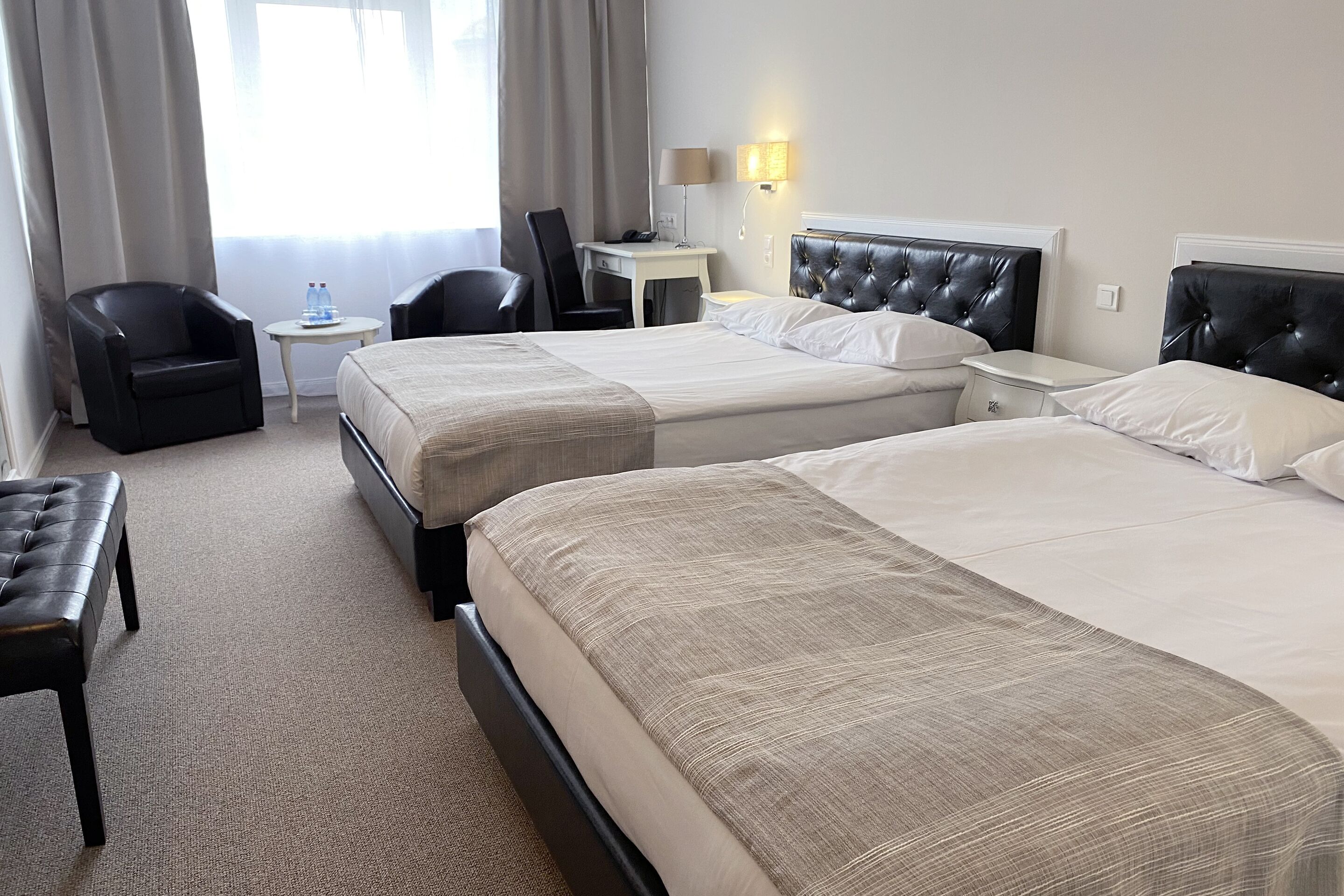 A hotel room with two beds, a desk, a chair, and a small table with a lamp.