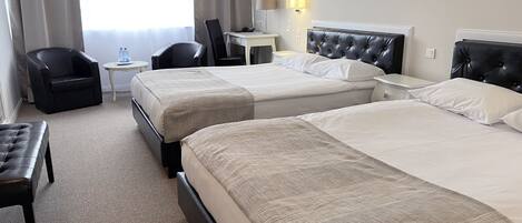 A hotel room with two beds, a desk, a chair, and a small table with a lamp.