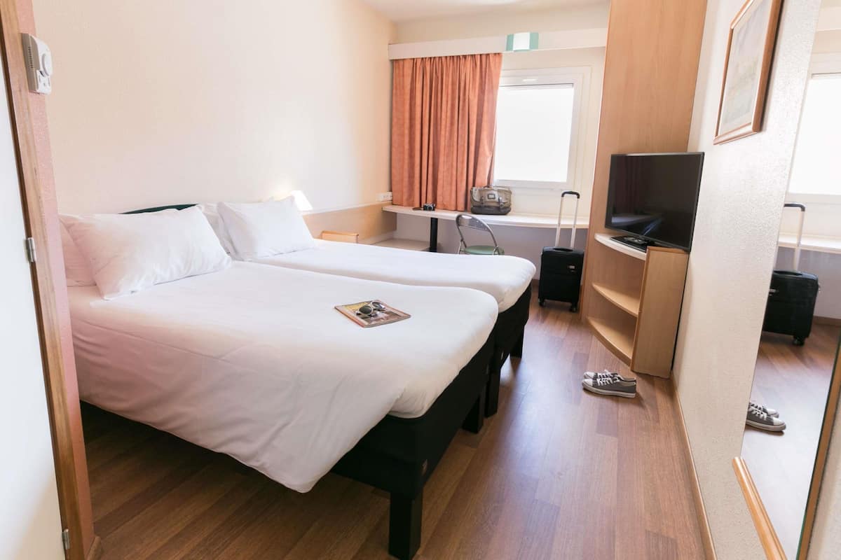Une chambre d’hôtel avec deux lits, une télévision, un bureau et une fenêtre avec des rideaux.