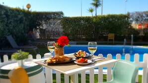 A dining table with a meal, two glasses of white wine, and a red flower centerpiece.