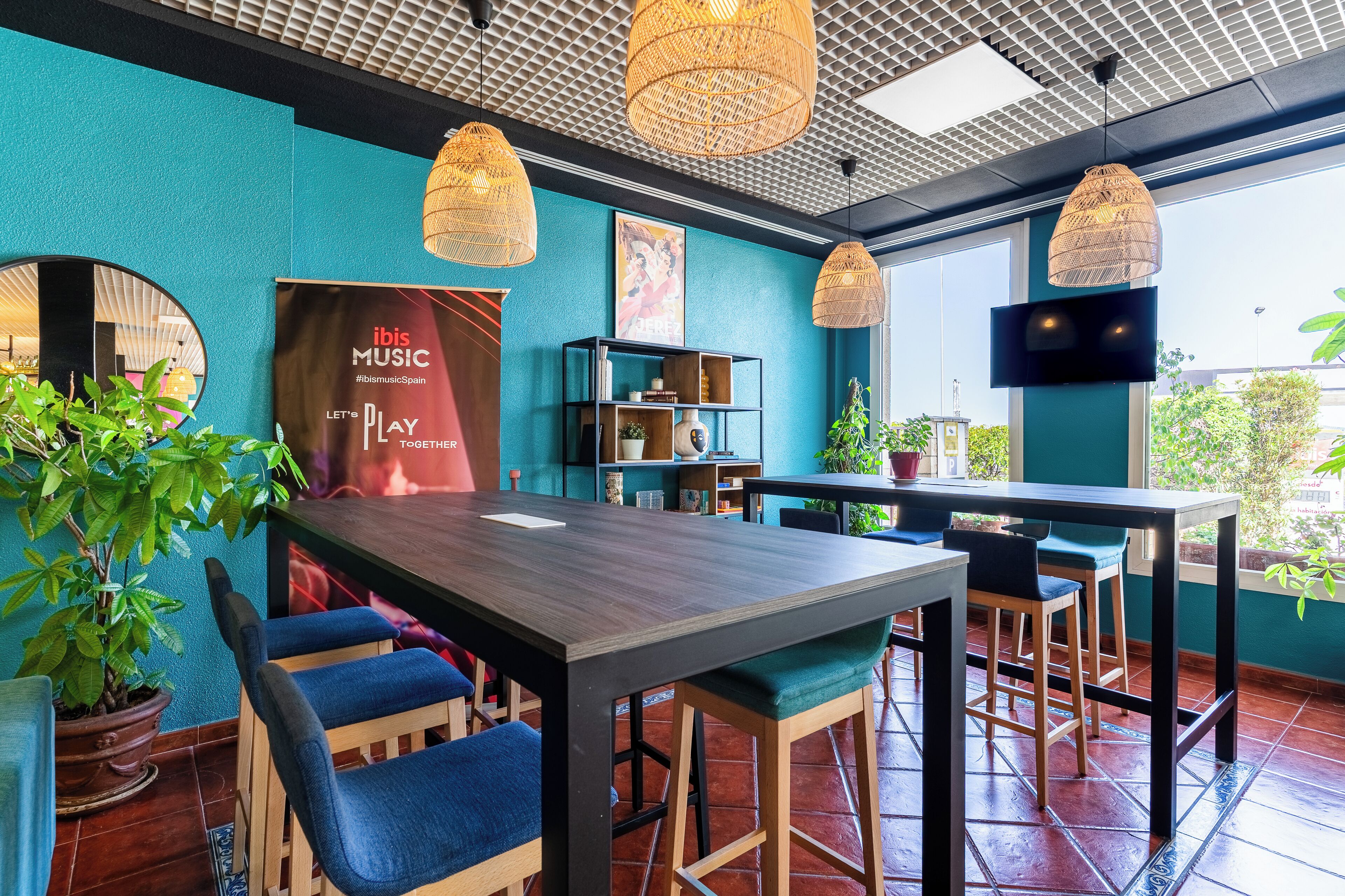 A restaurant with a wooden table, blue chairs, wicker pendant lights, and a large window.