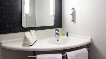 A bathroom with a white sink, a mirror, a towel rack, and a soap dispenser.