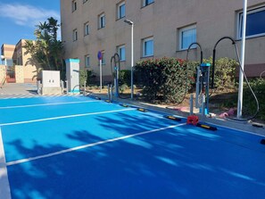 A blue parking area with electric vehicle charging stations, a building with multiple windows, and a clear sky. - ibis Jerez de La Frontera (Jerez de la Frontera)