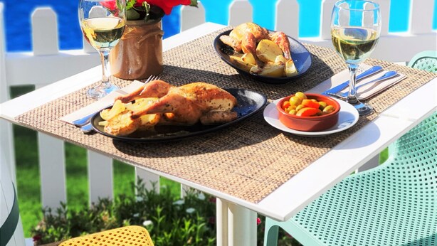 A dining table with a meal, a glass of white wine, and a vase with a red flower.