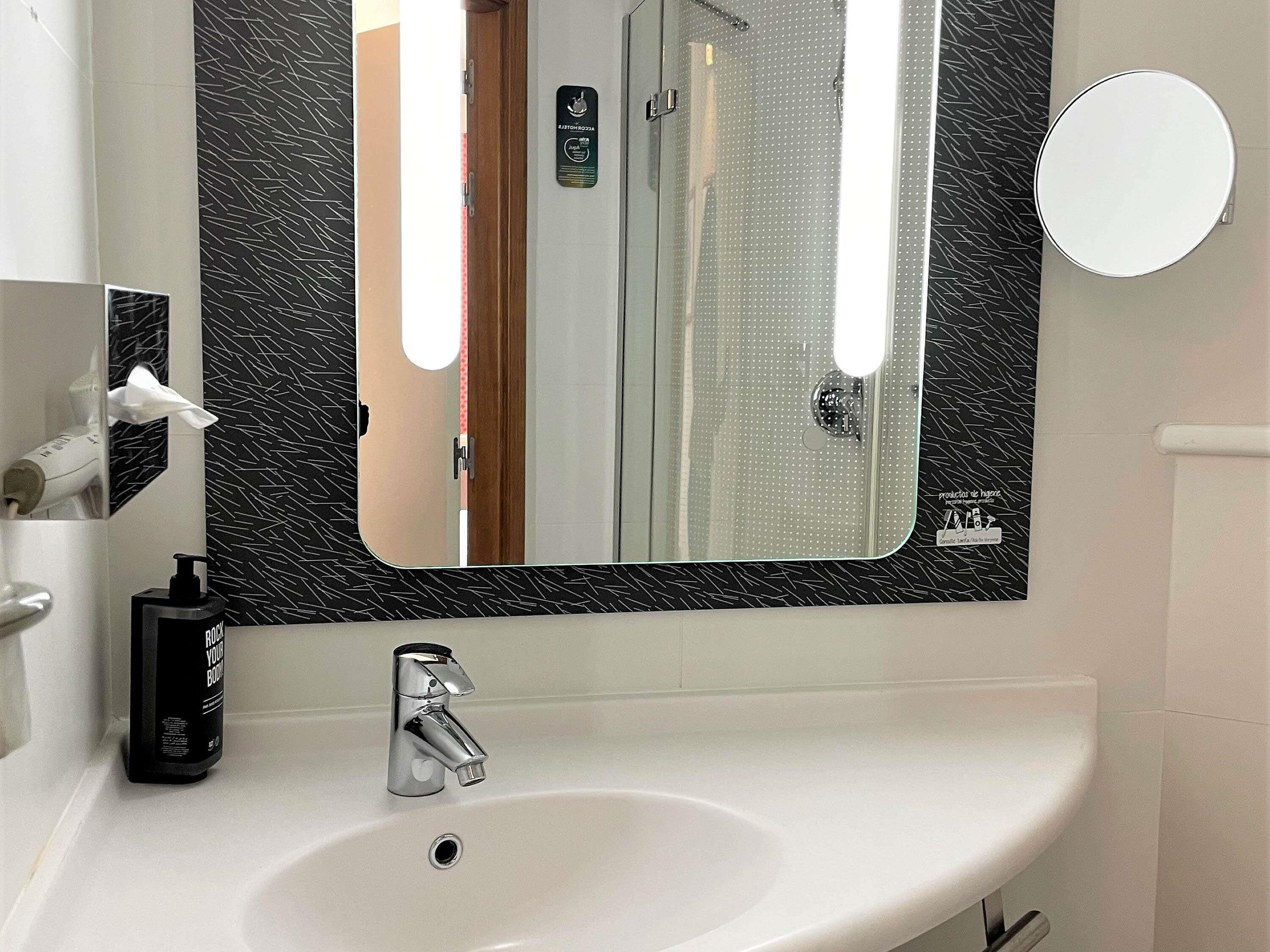 A bathroom with a white sink, a mirror, a soap dispenser, and a towel dispenser.