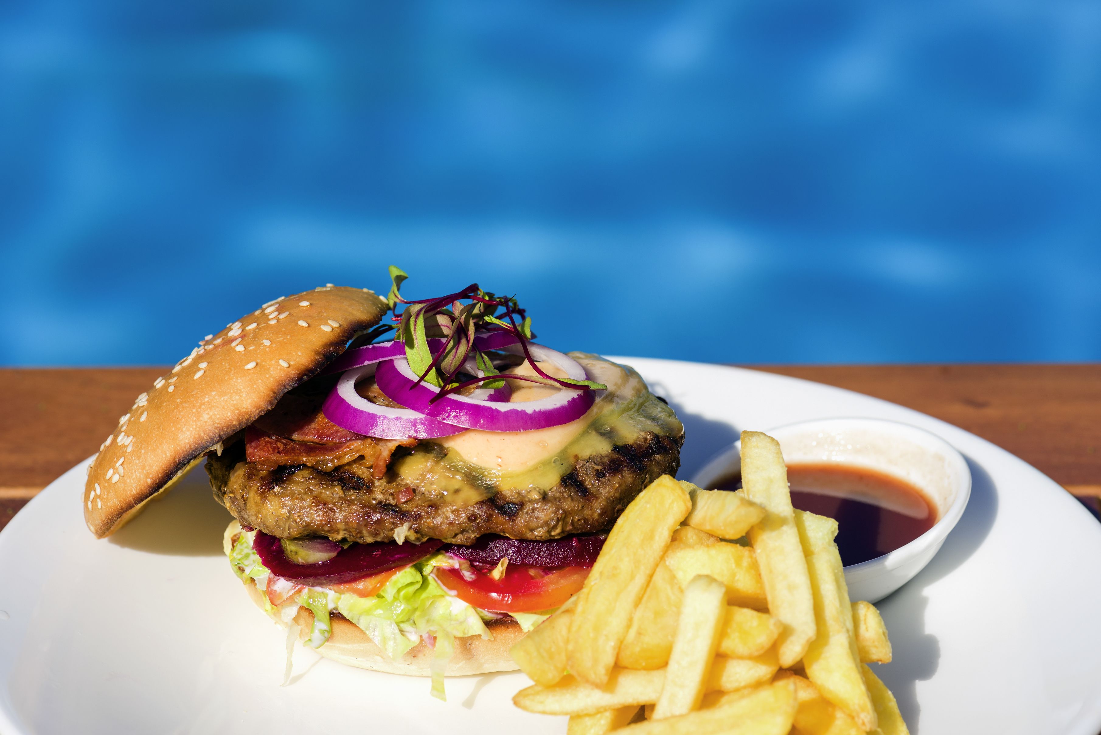 A burger with fries and a side of sauce on a white plate.