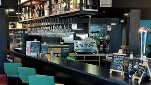 A bar area with multiple stools, a coffee machine, and shelves stocked with bottles.