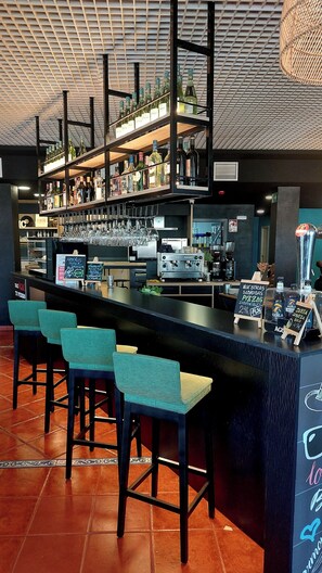 Een bar met meerdere krukken, een koffieapparaat en planken vol flessen.