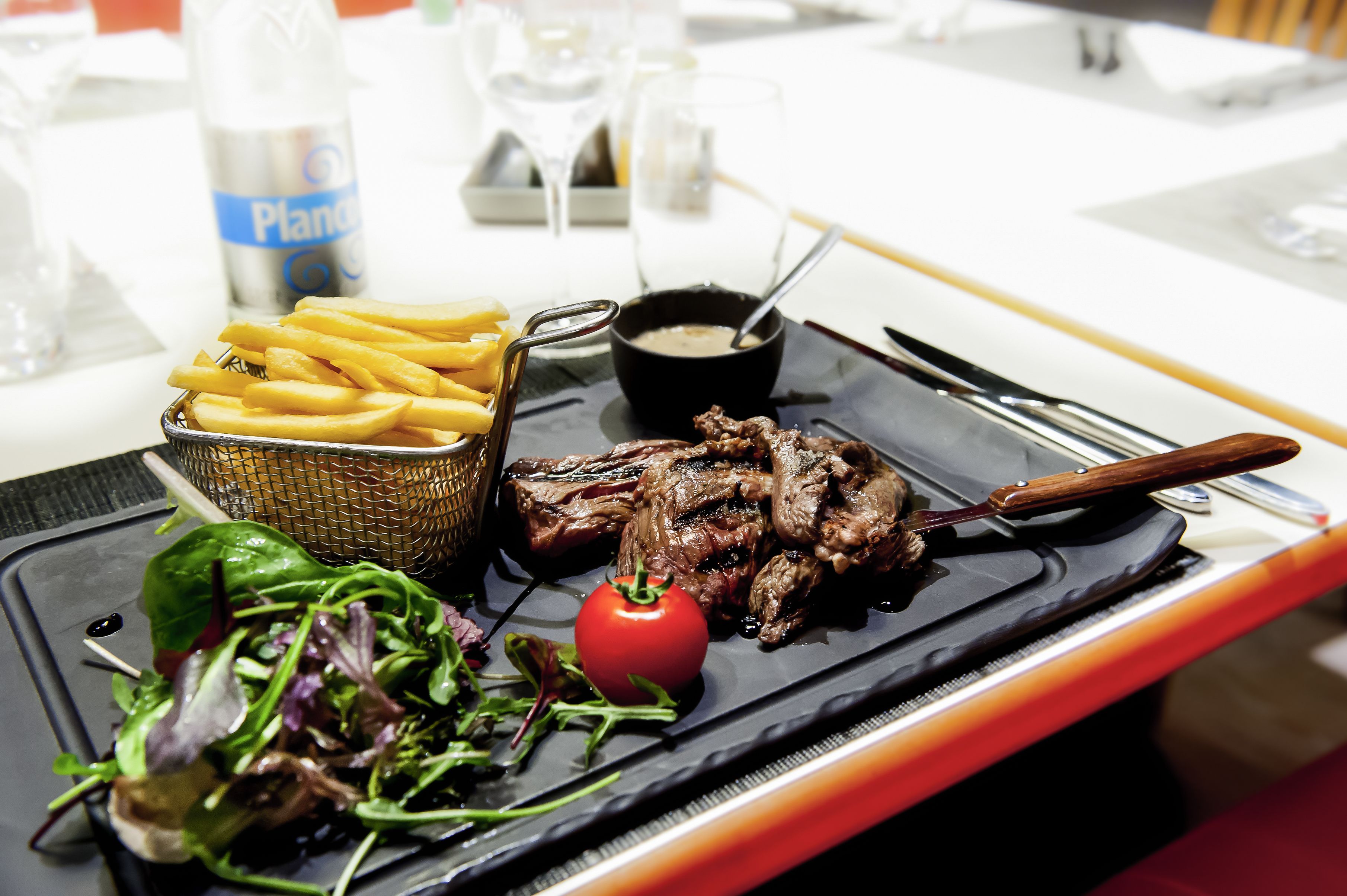 Uma refeição com bife, batatas fritas e salada em um prato preto.