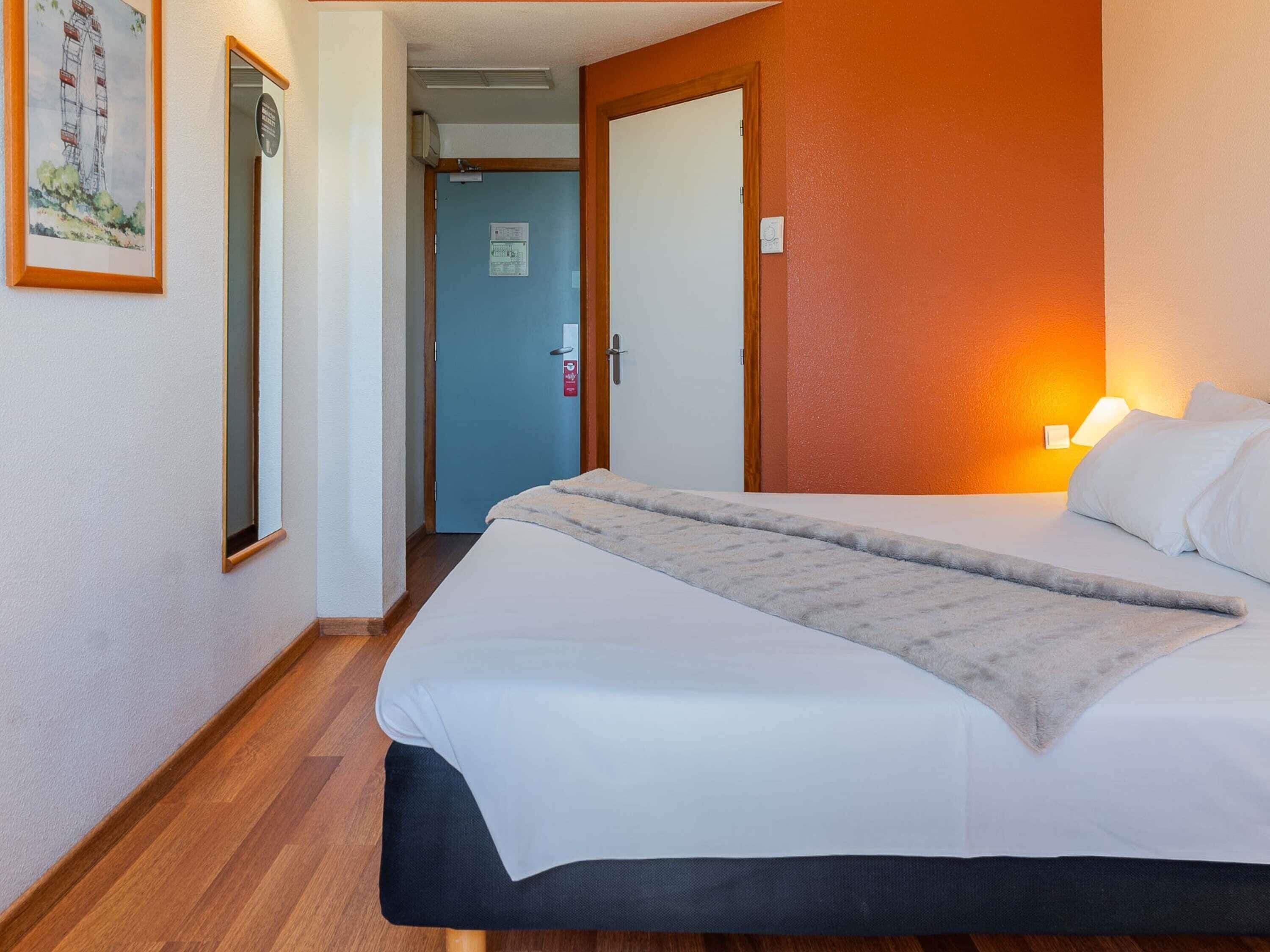 Une chambre d’hôtel avec un lit, une lampe de chevet, une porte et un couloir.