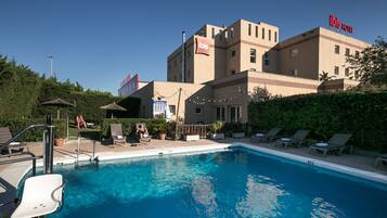 A hotel with a swimming pool, outdoor seating, and a sign for the ibis hotel.
