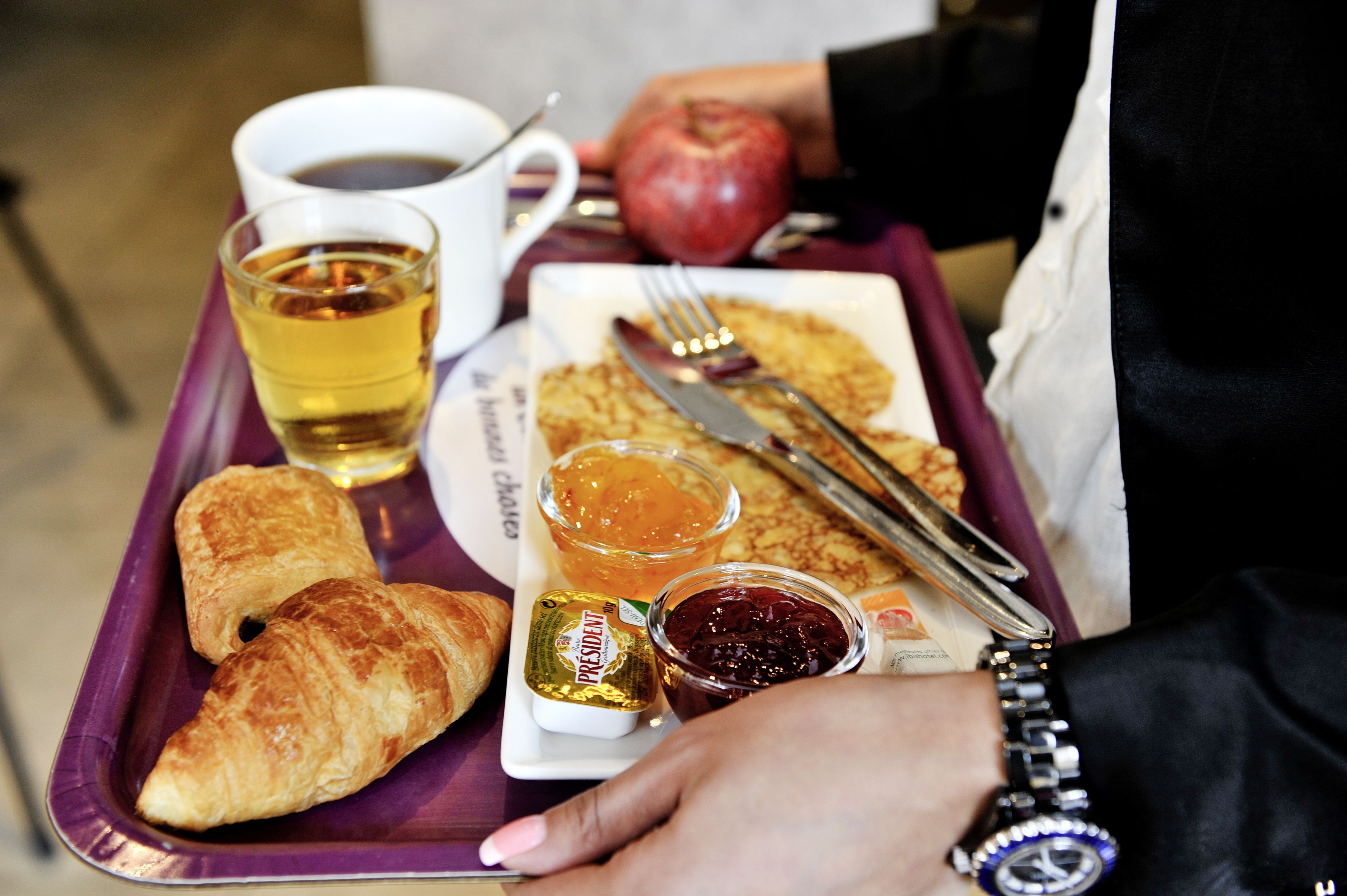 Ein Tablett mit Croissants, einer Kaffeetasse, einem Apfel und Beilagen.