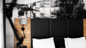 A hotel room with a bed, a nightstand, a lamp, and a wall-mounted picture of a cityscape.