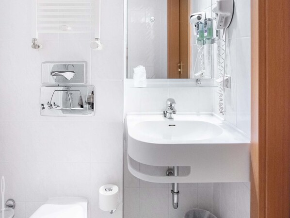 A bathroom with a sink, mirror, towel dispenser, and toilet.