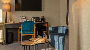 Habitación de hotel con televisión de pantalla plana, escritorio con cafetera, una silla azul, una mesa de madera y un sofá.