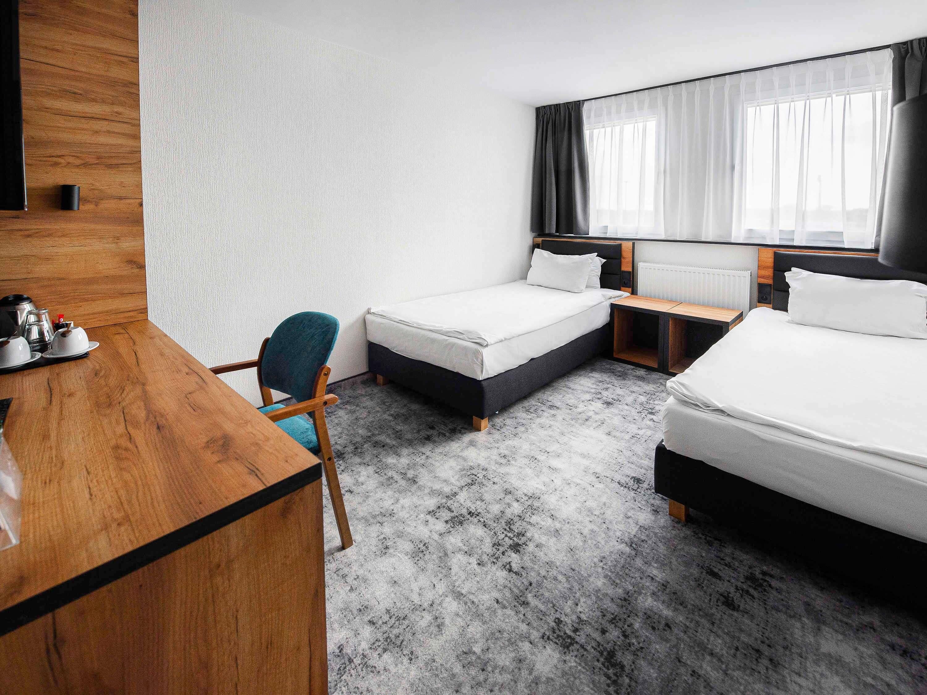 A hotel room with two beds, a desk, a chair, and a large window with curtains.