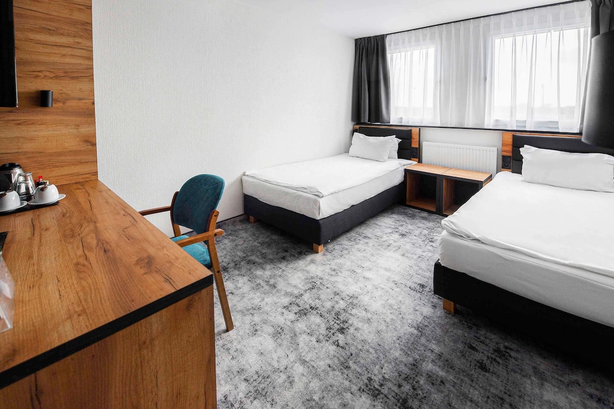 A hotel room with two beds, a desk, a chair, and a large window with curtains.