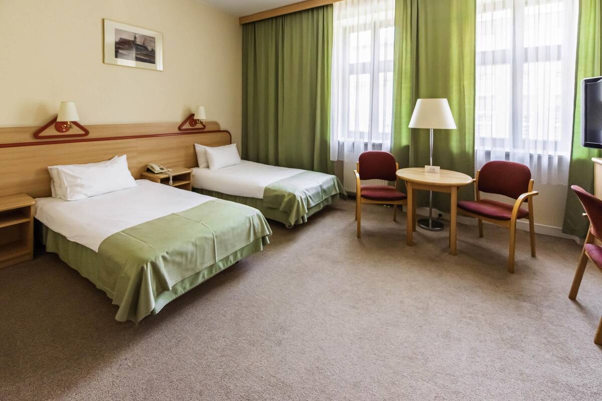 Una habitación de hotel con dos camas, un escritorio, una silla, un televisor y una ventana con cortinas.