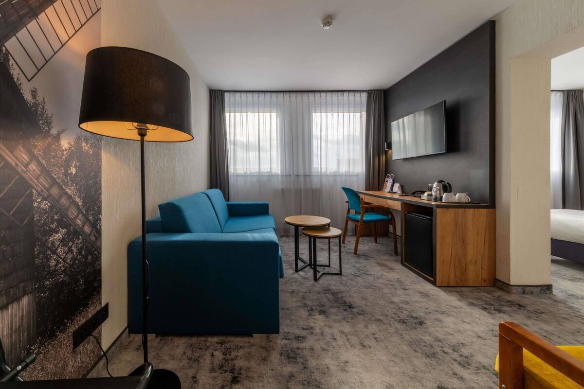 Una habitación de hotel con un sofá, un escritorio, una silla, un televisor y una lámpara.
