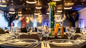 A dining area with round tables set with fine china, silverware, and wine glasses.