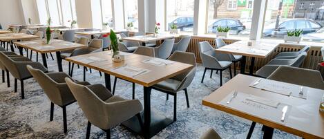 Un vaste espace dédié à la salle à manger, avec de nombreuses tables et chaises, de grandes fenêtres et une vue sur la rue.