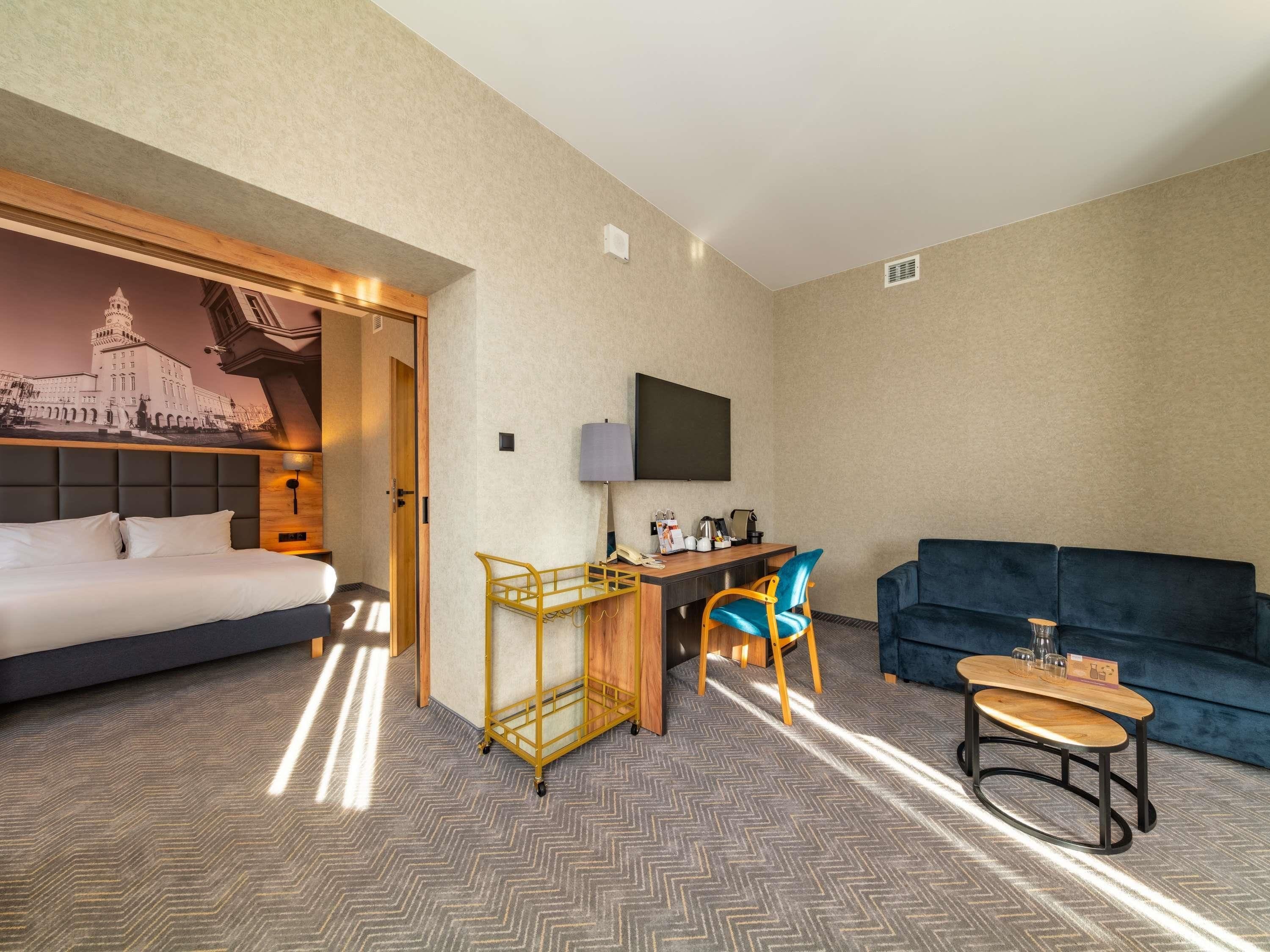 A hotel room with a bed, desk, chair, TV, and a couch.