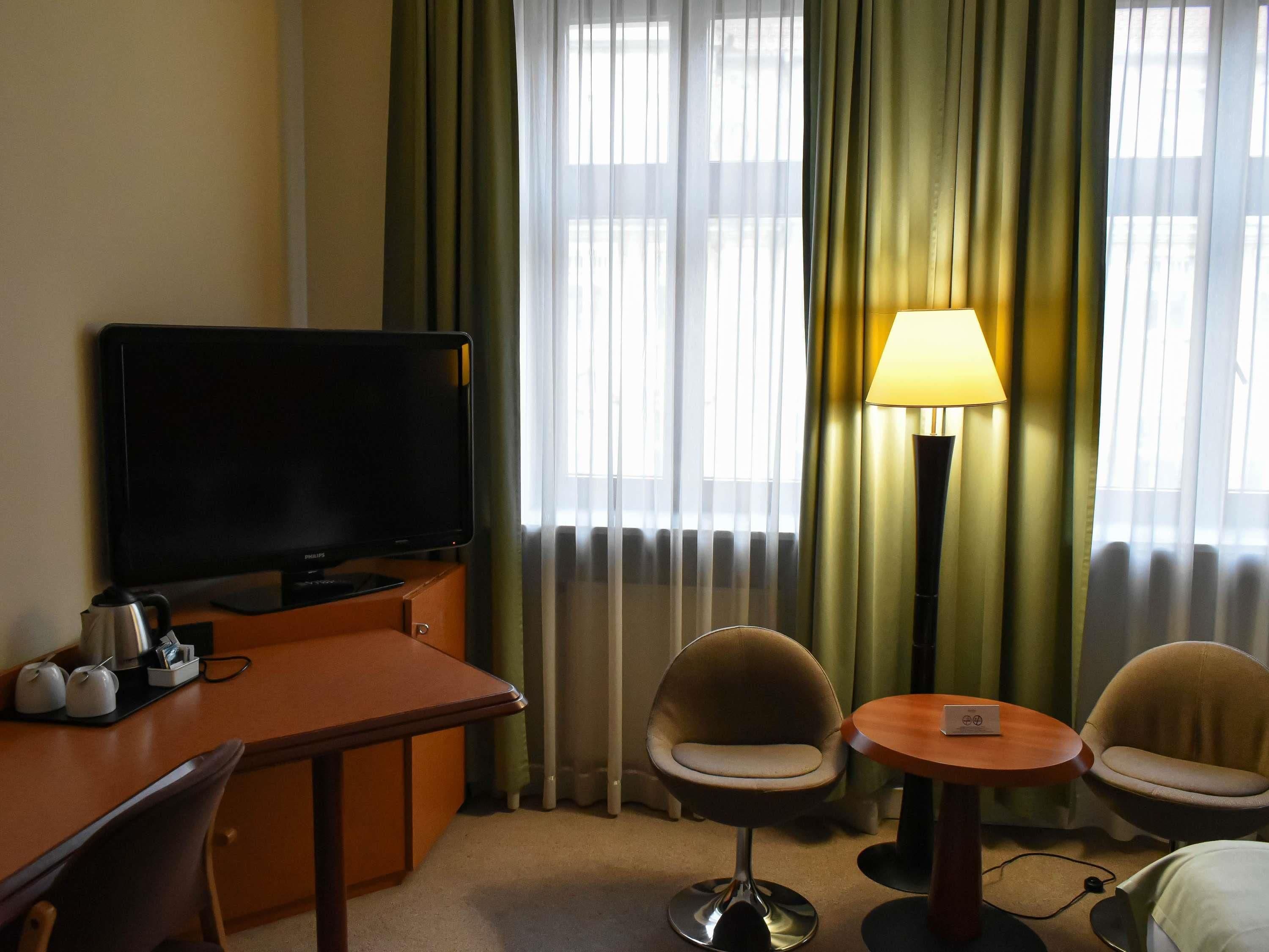 A hotel room with a television, two chairs, a small table, and a lamp.