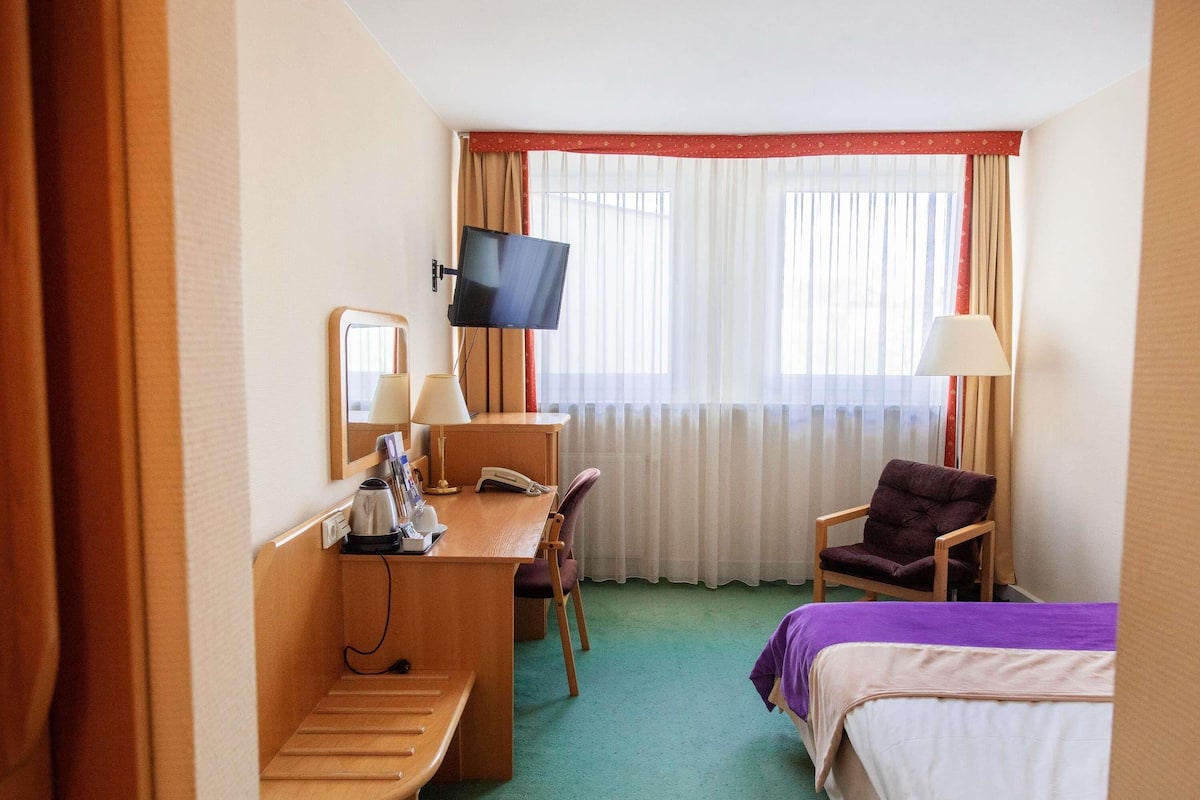 Habitación de hotel con escritorio, silla, cama, televisión y cortinas.
