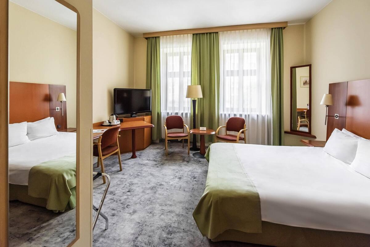 Una habitación de hotel con cama, escritorio, sillas, televisor y espejo.