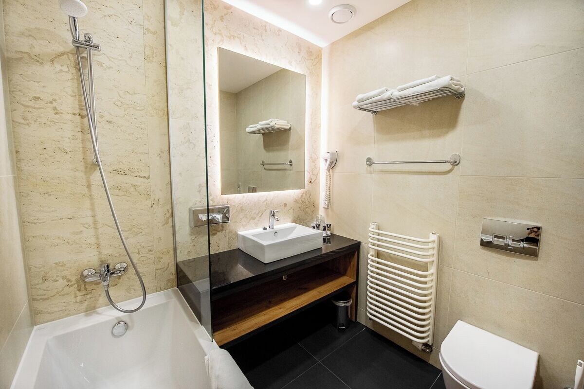 A modern bathroom with a bathtub, a sink, a mirror, a towel rack, and a toilet.