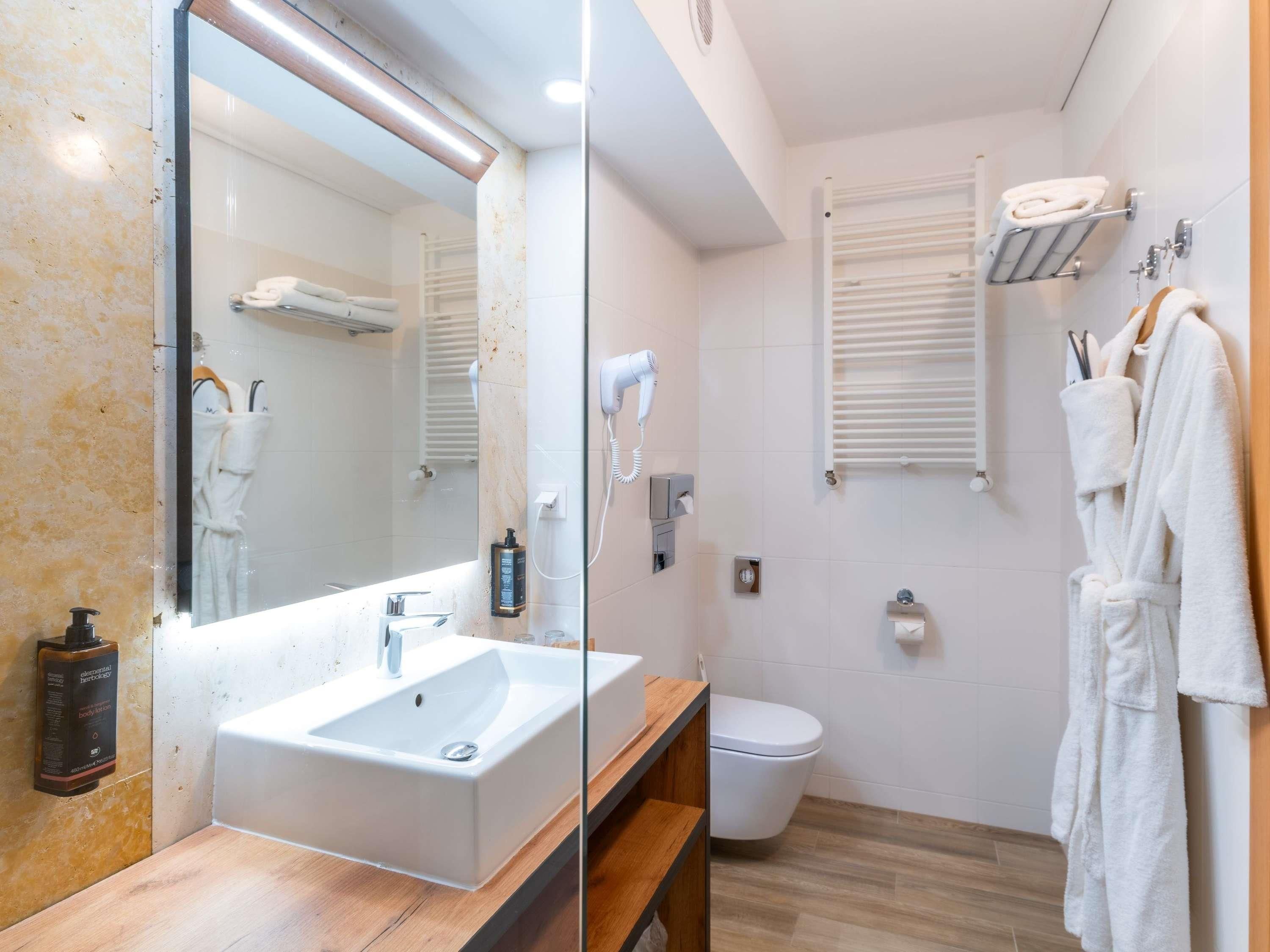 A modern bathroom with a large mirror, a sink, a toilet, and a shower area.