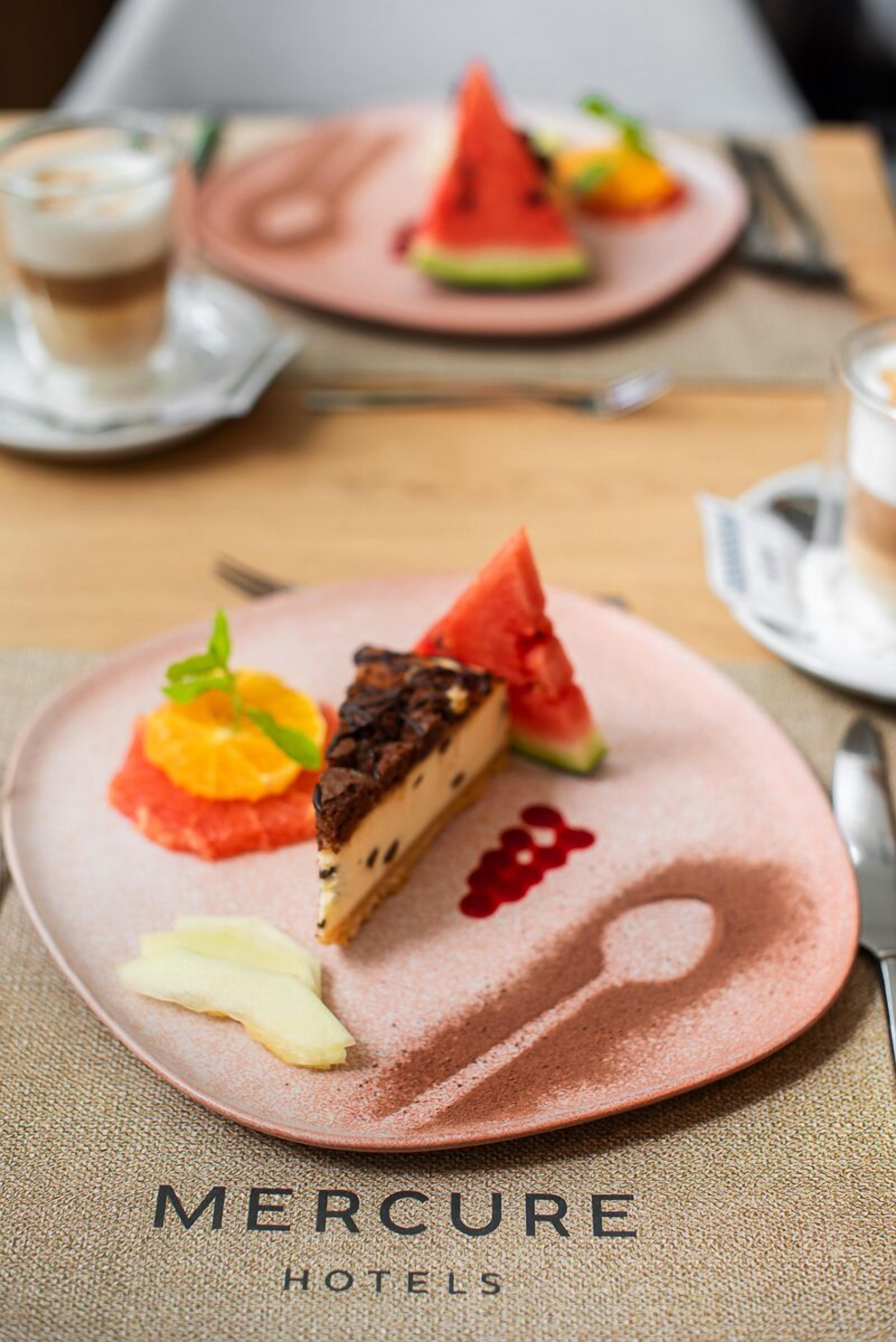 A dessert plate with a slice of cheesecake, watermelon, and orange garnish on a pink plate.