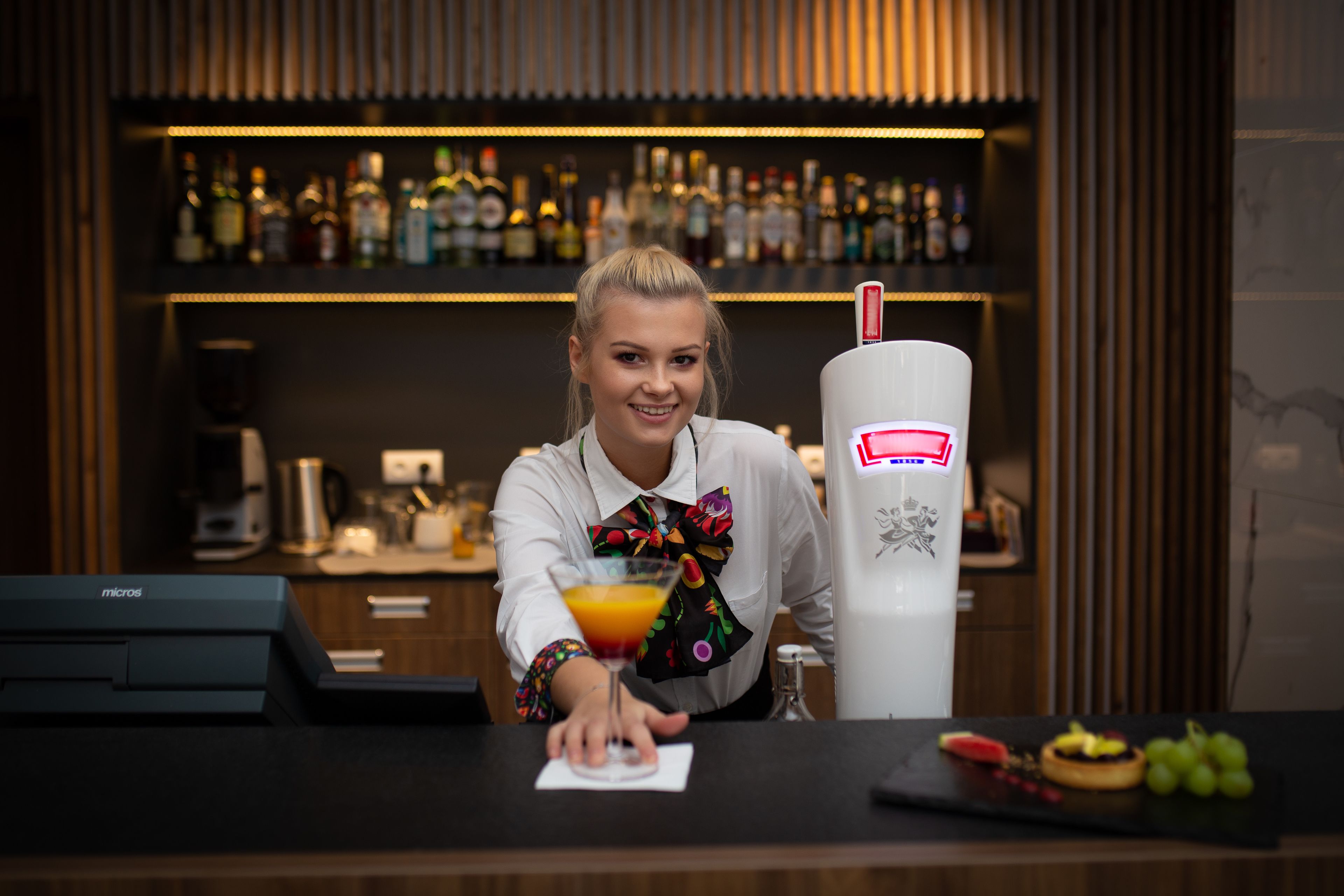 A bar area with a bartender, a cocktail, and a selection of bottles on shelves.